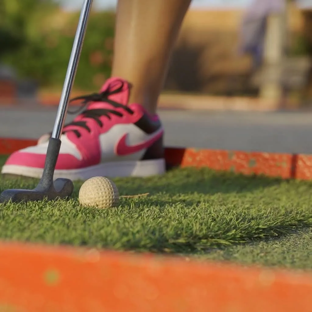 Un chico jugando a minigolf en un dia soleado.